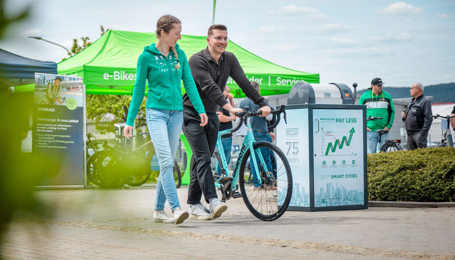 Deux personnes avec un vélo bleu clair lors d'un événement de vélos électriques en plein air, sous une tente verte et avec un panneau d'affichage.