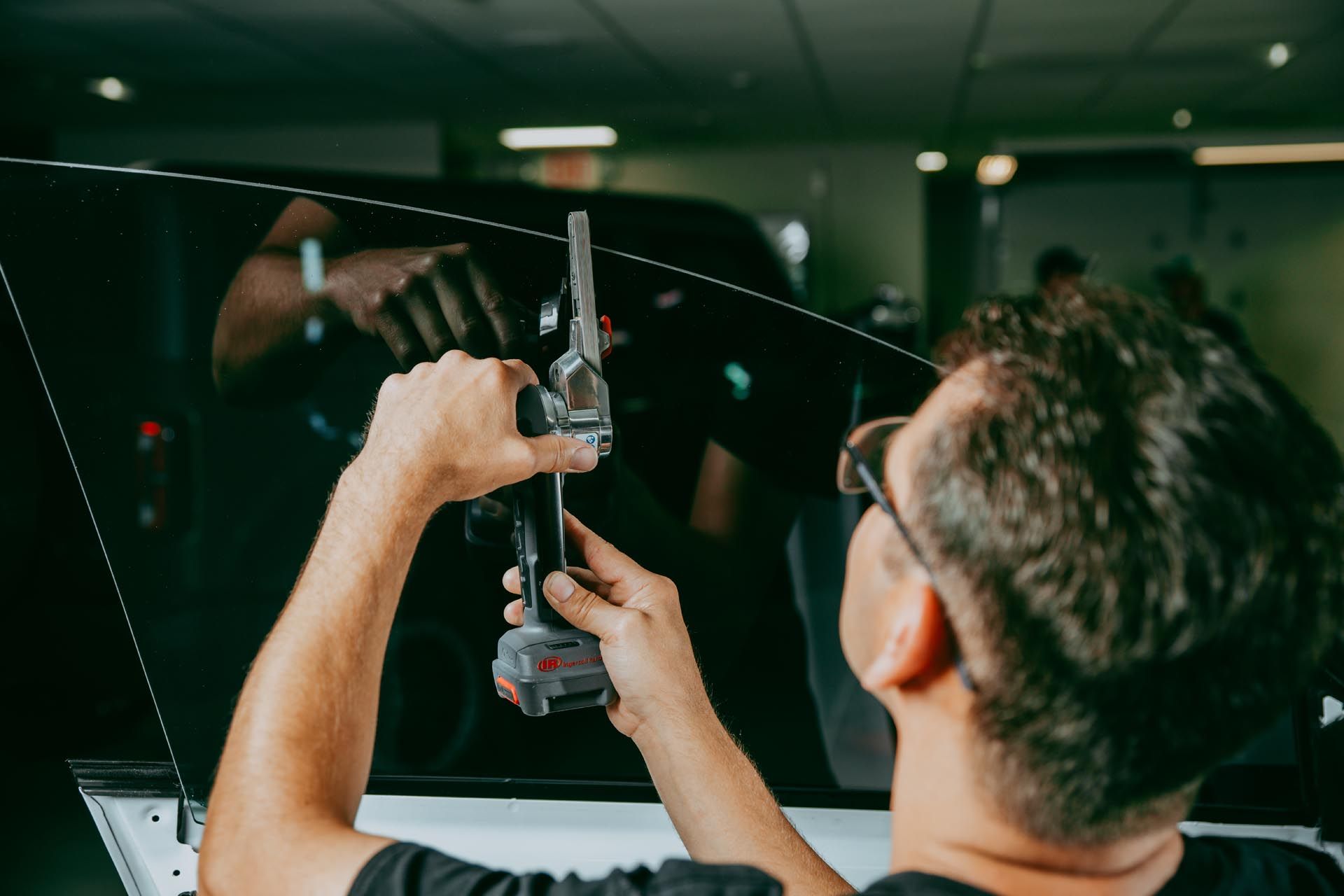 A man is working on a car window with a drill.