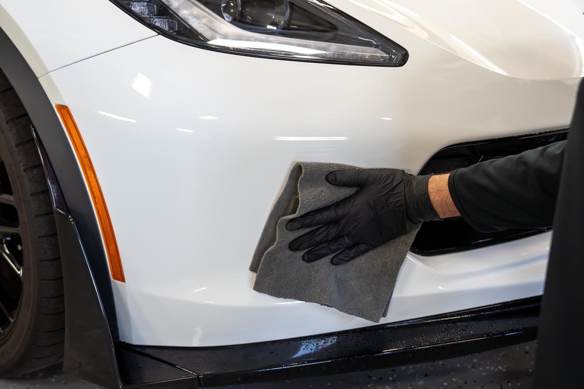 Person in black gloves wiping white car bumper with a gray cloth.