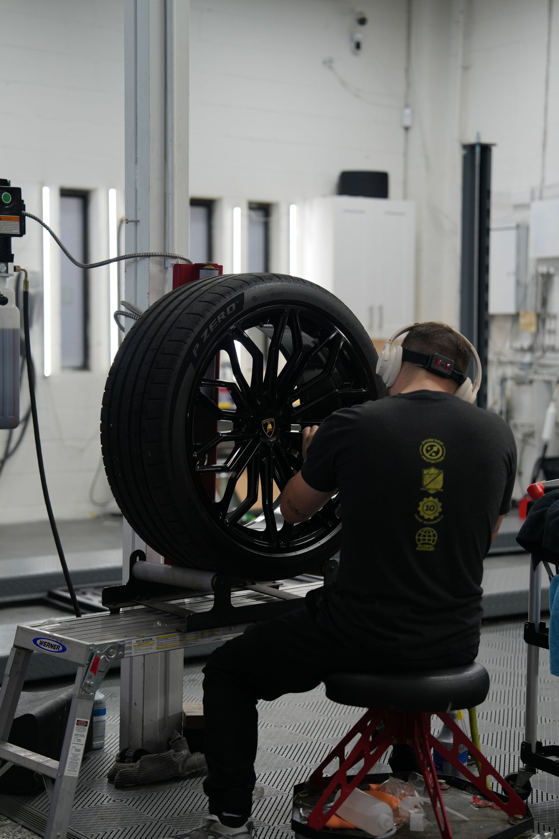 Mechanic working on a black car wheel in a workshop.