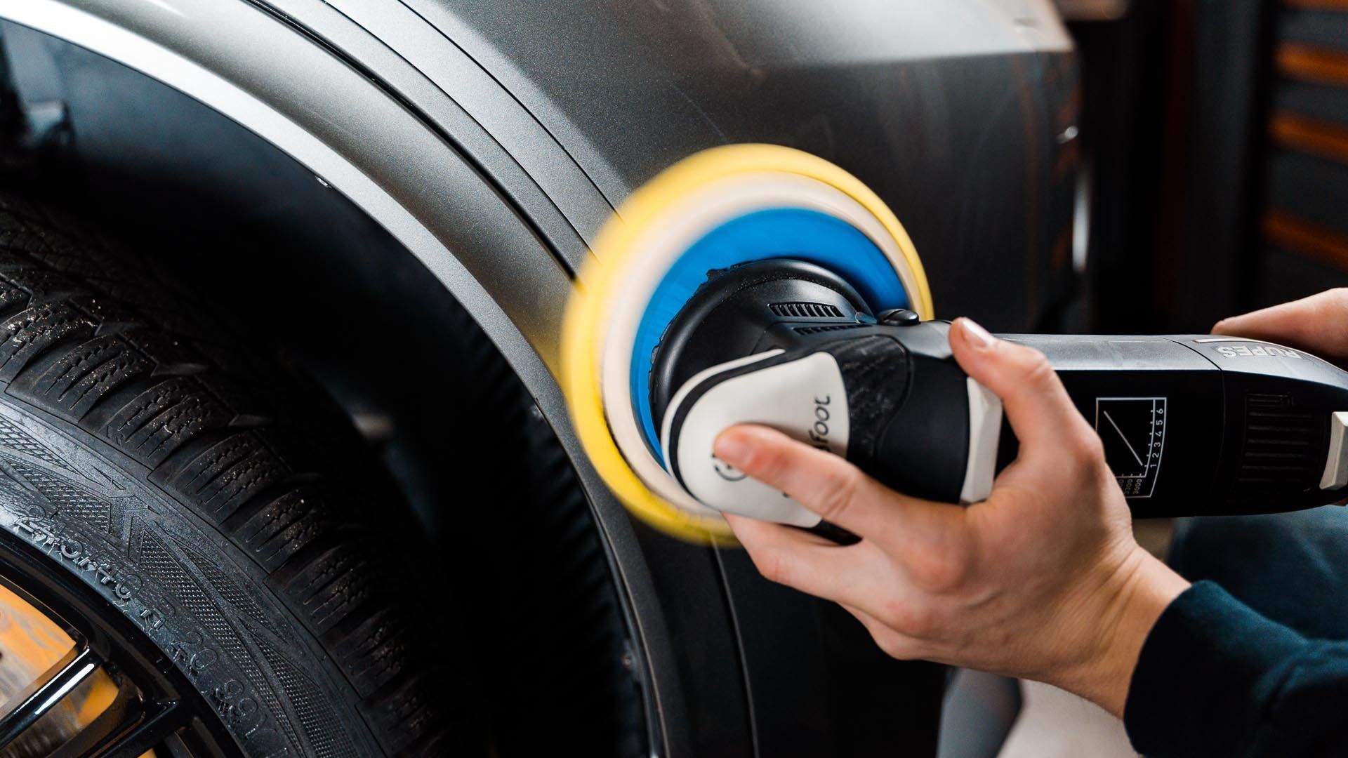 Person using a polisher on a car's fender, removing scratches. Yellow and blue polishing pad.