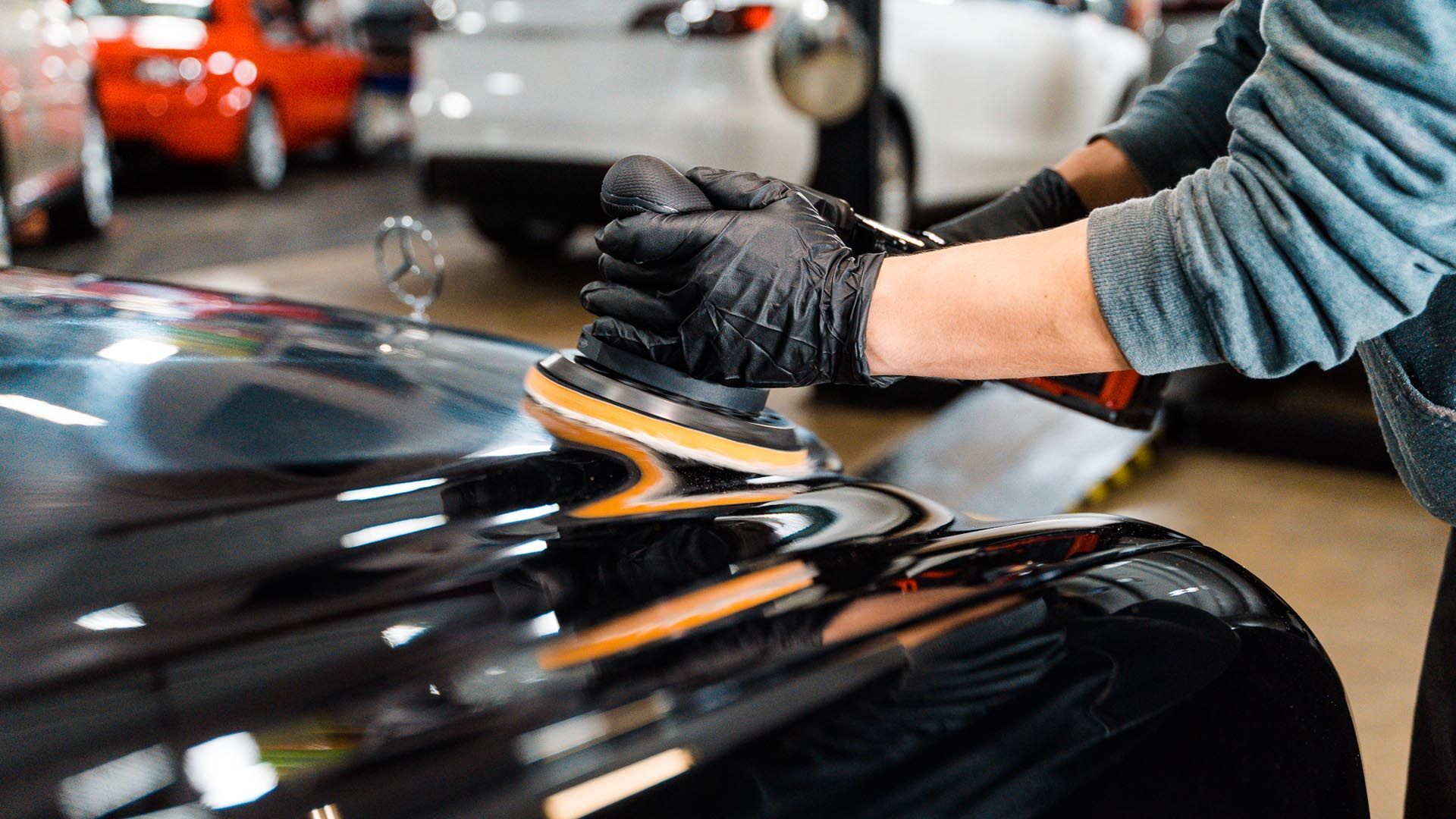A man is polishing the hood of a black car in a garage.