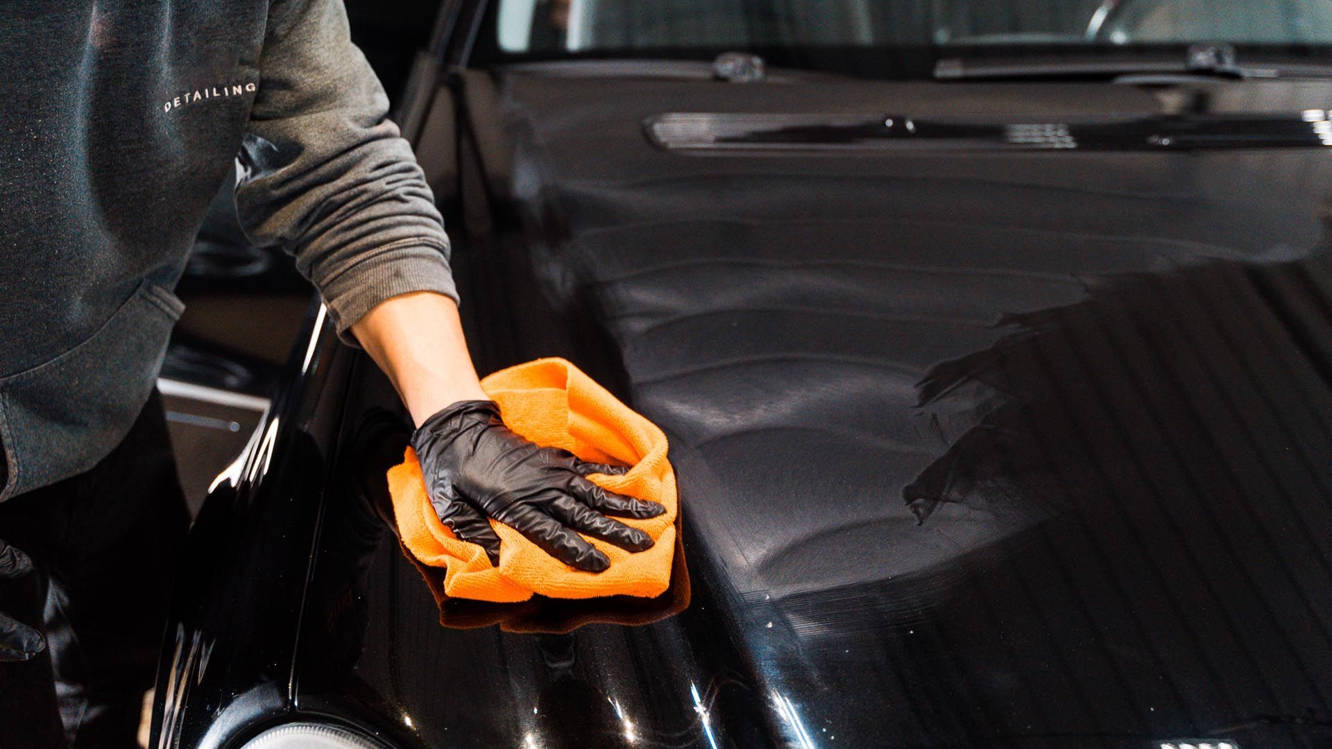 Person wearing a black glove wiping a black car with an orange cloth.