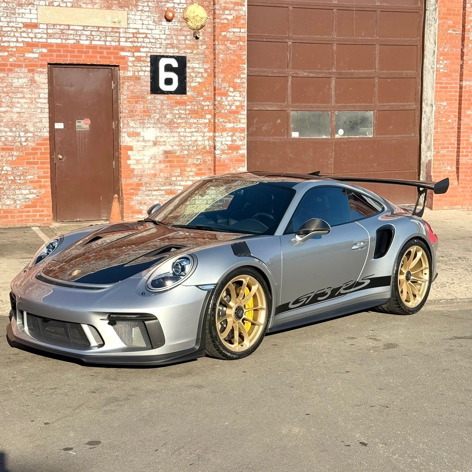A silver porsche 911 gt3 rs is parked in front of a brick building.