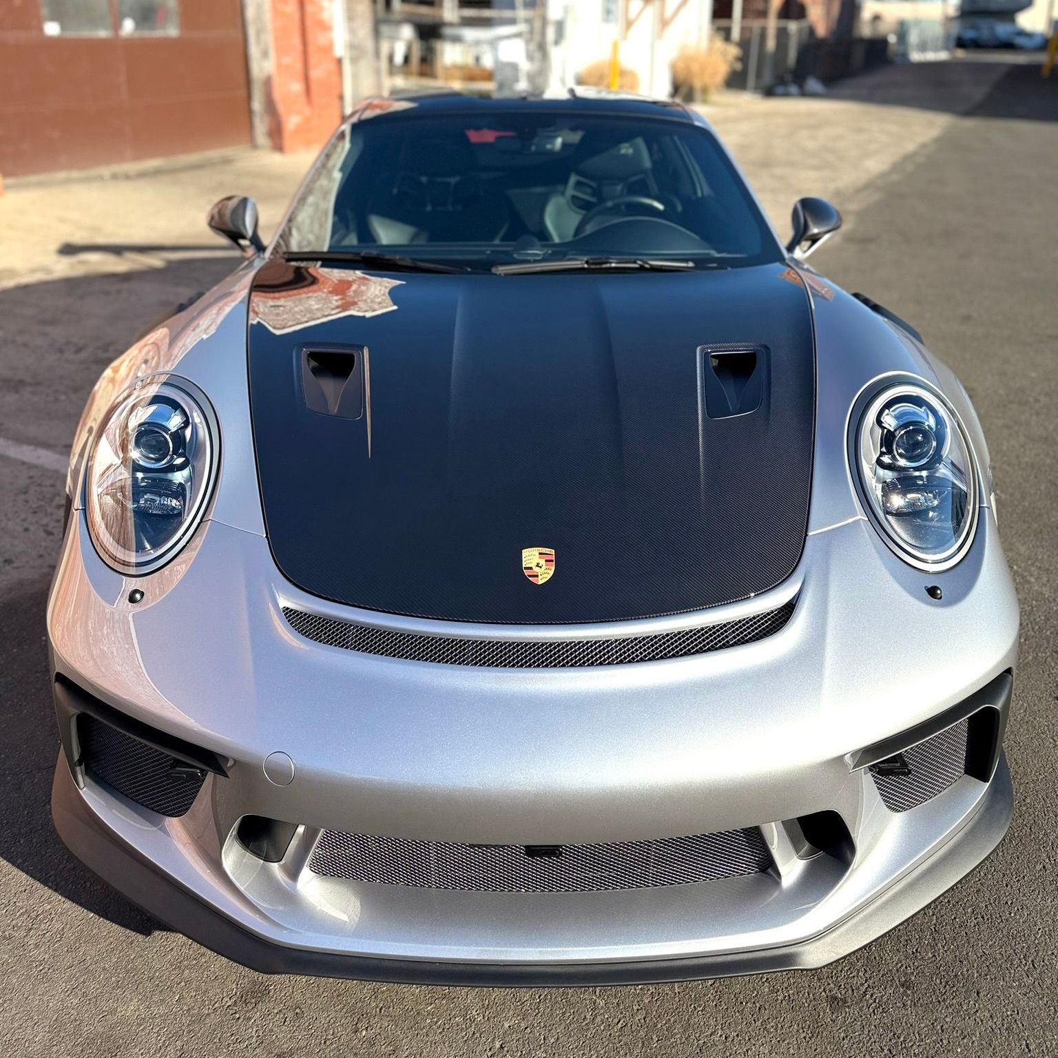 A silver porsche 911 gt3 rs is parked in front of a garage.