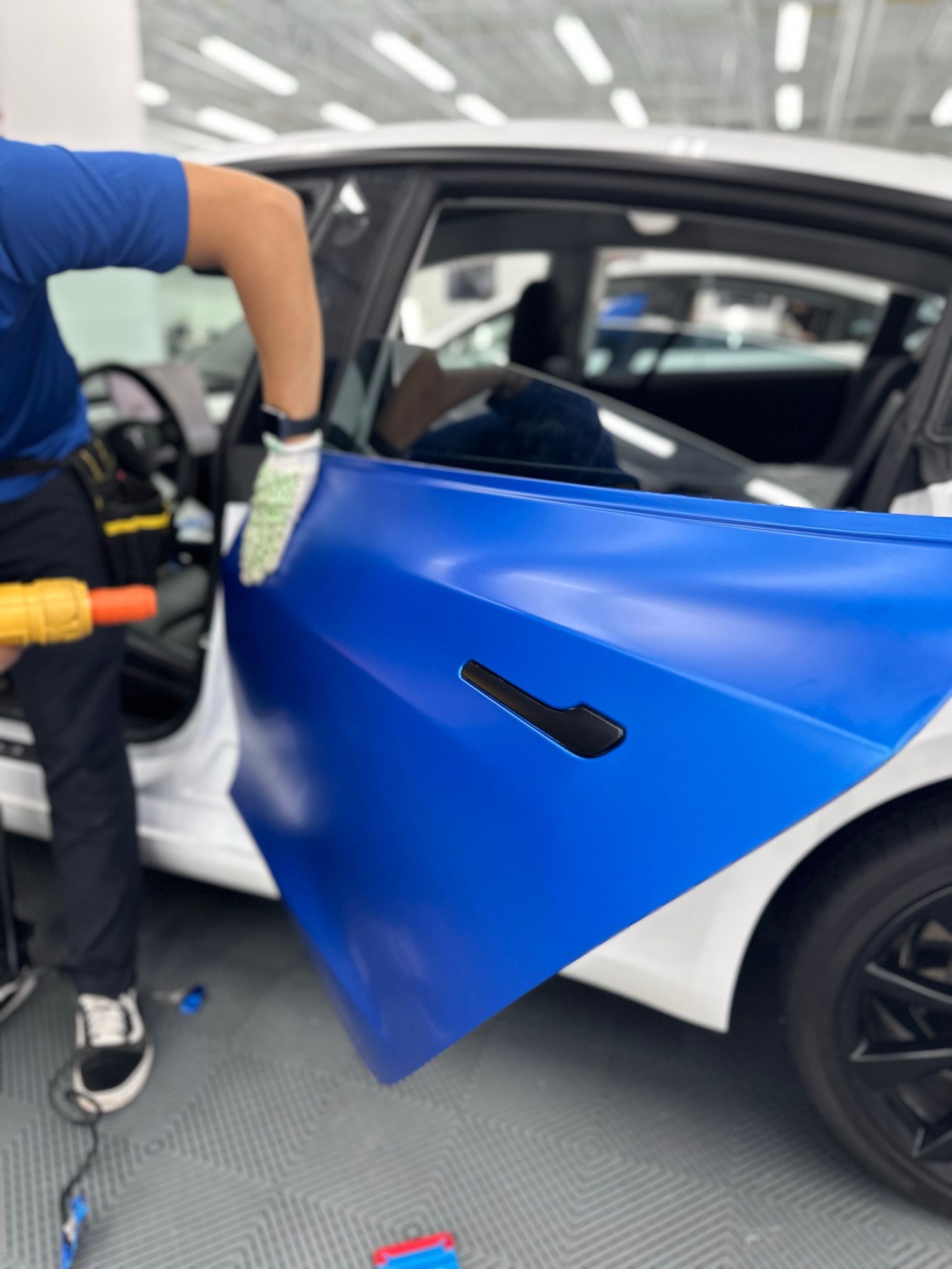A man is wrapping a blue and white car with a drill.