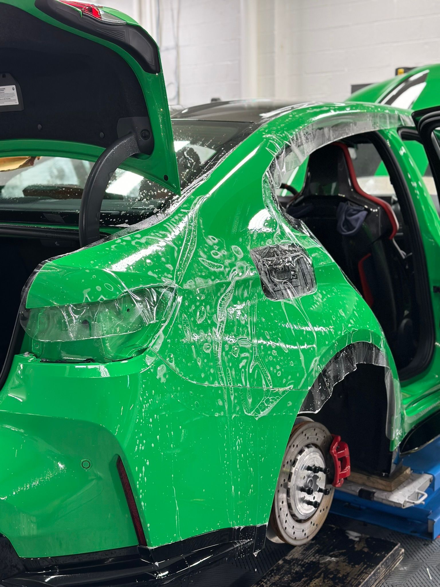 Green sports car, partially disassembled, in a workshop. Red brake calipers visible.