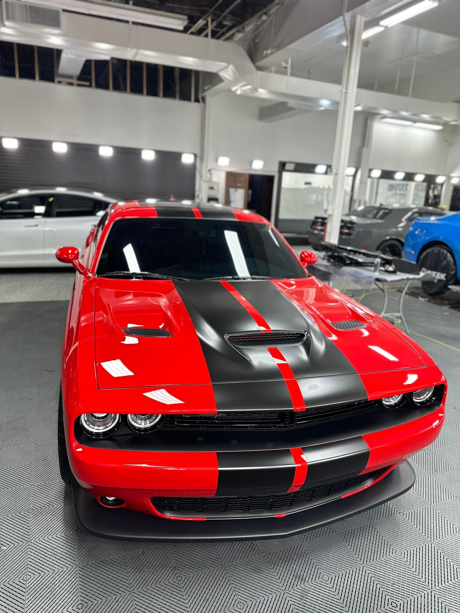 Red Dodge Challenger with black racing stripes in a garage setting.