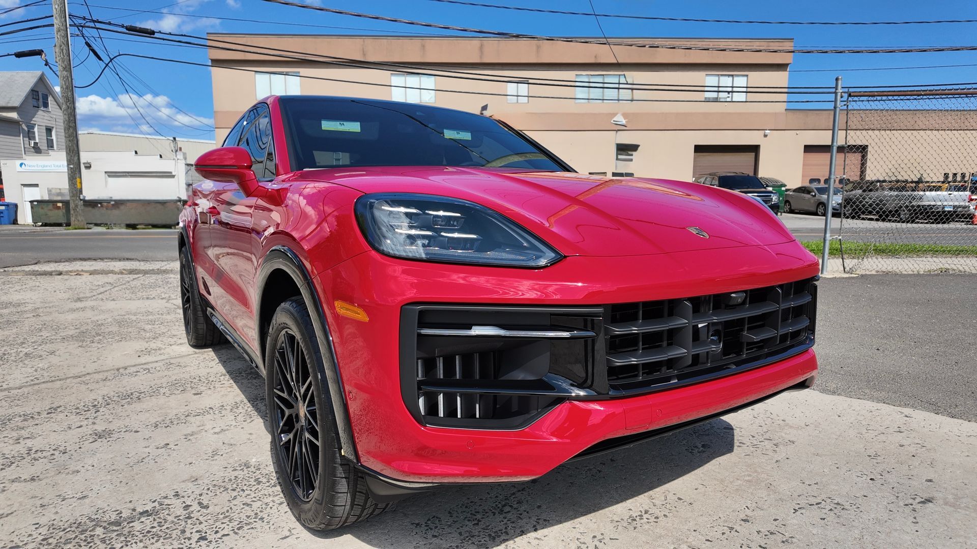 Red Porsche SUV parked outside a commercial building on a sunny day.
