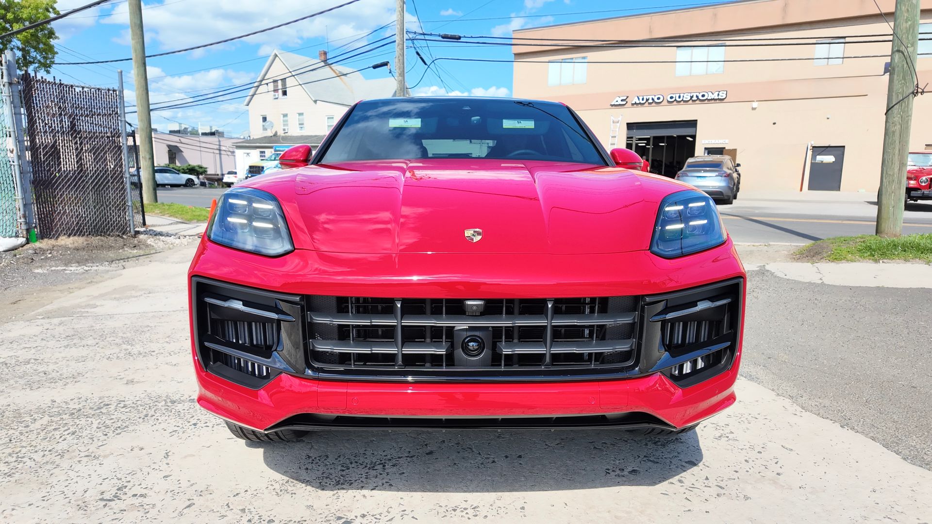 Red Porsche SUV parked on the street, front view. Building background, sunny day.