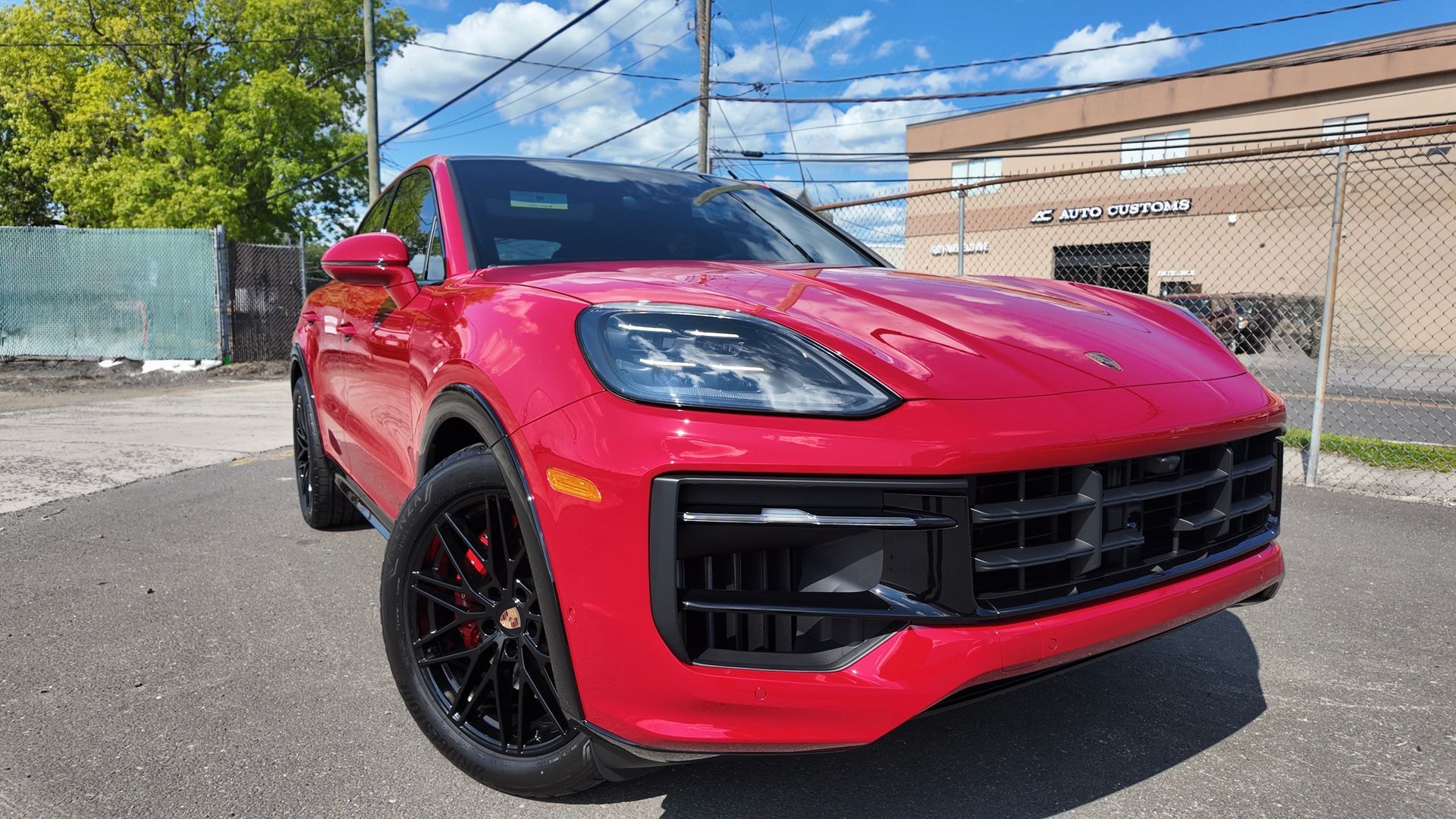 Red Porsche SUV parked outside on a sunny day. Black wheels, dark front grille, and a building in the background.