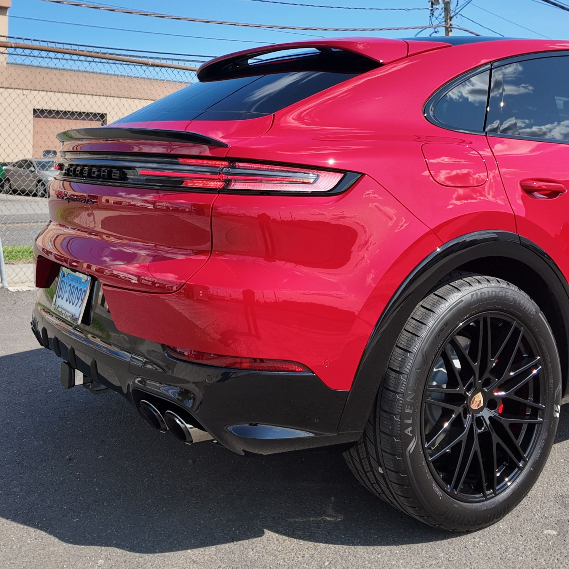 Red Porsche SUV parked on a sunny street, black wheels, spoiler, and trim.