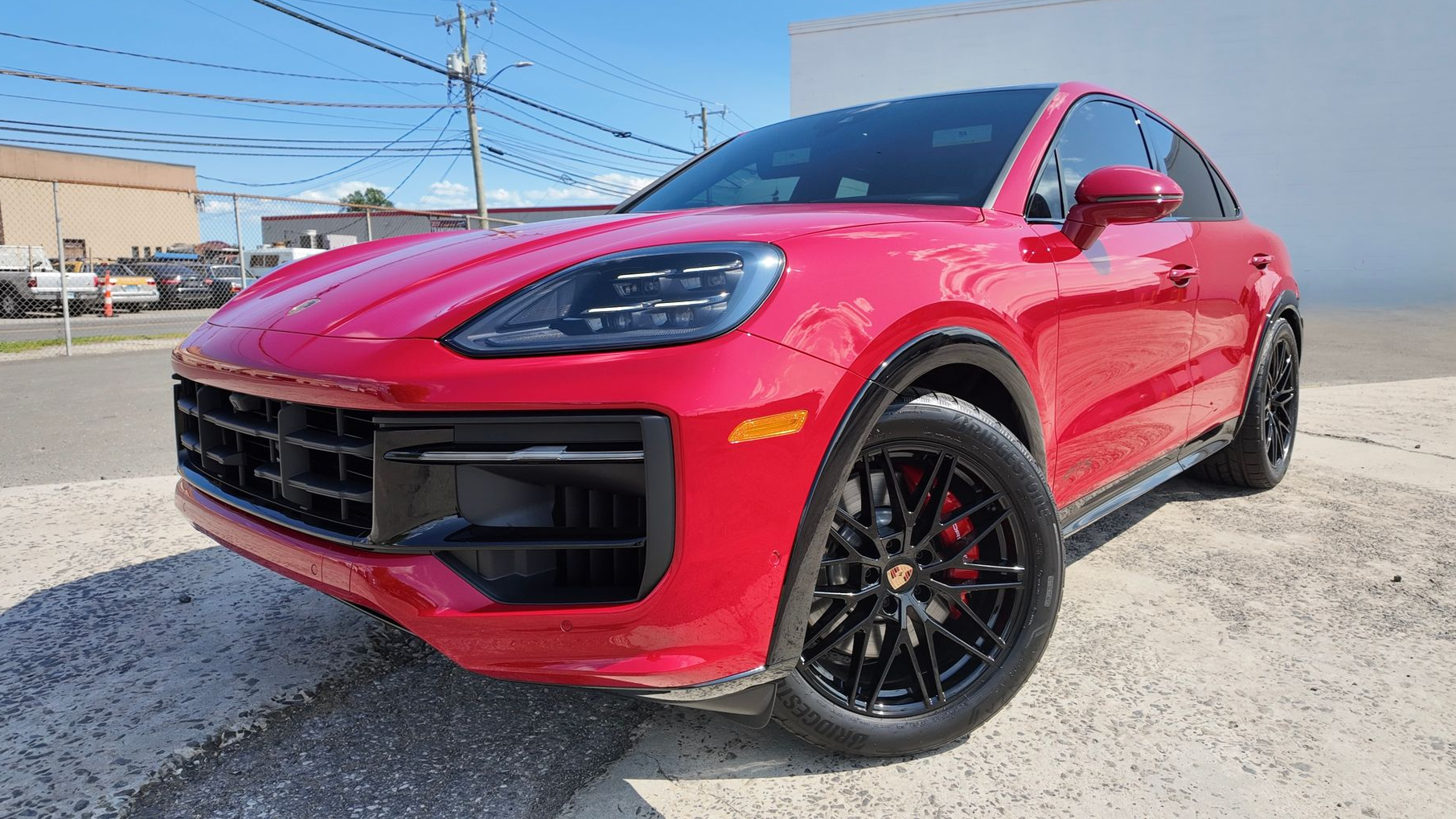 Red Porsche SUV parked on a street, black wheels, bright sunny day.