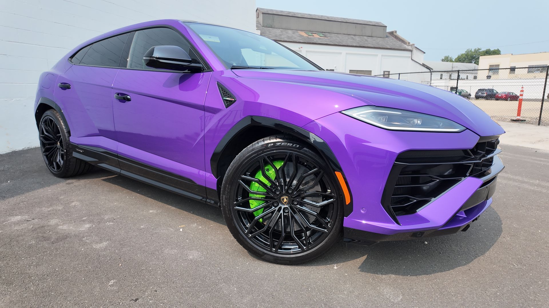 Purple Lamborghini Urus SUV with green brake calipers, parked outside.
