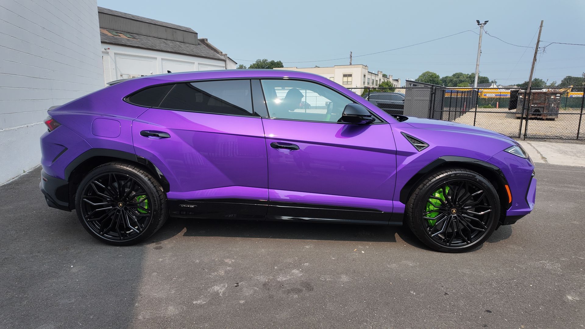 Purple Lamborghini SUV with black wheels and green brake calipers, parked outside.