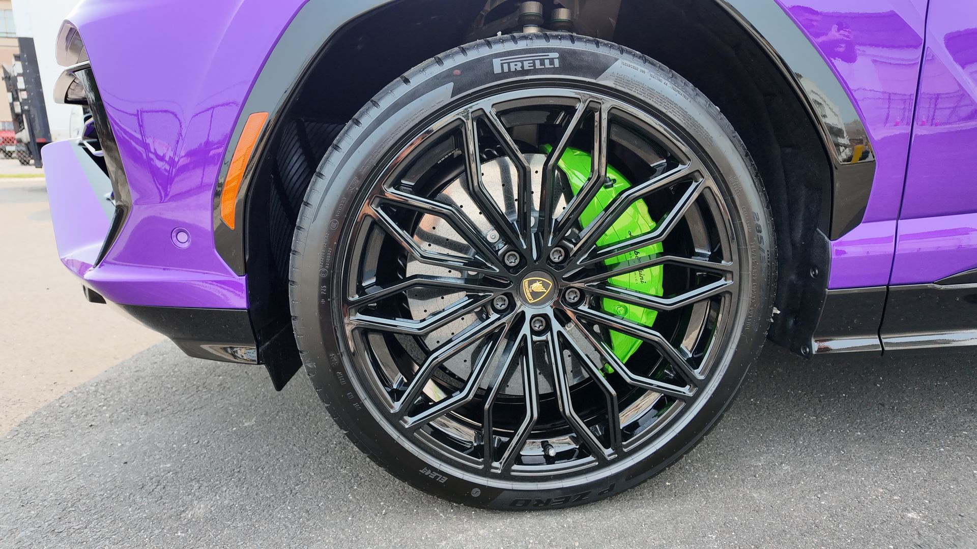 Purple Lamborghini SUV wheel with black rims, green brake calipers.