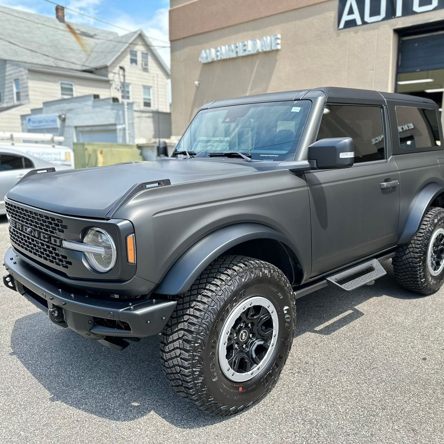 Gray Ford Bronco parked outside a car repair shop on a sunny day.