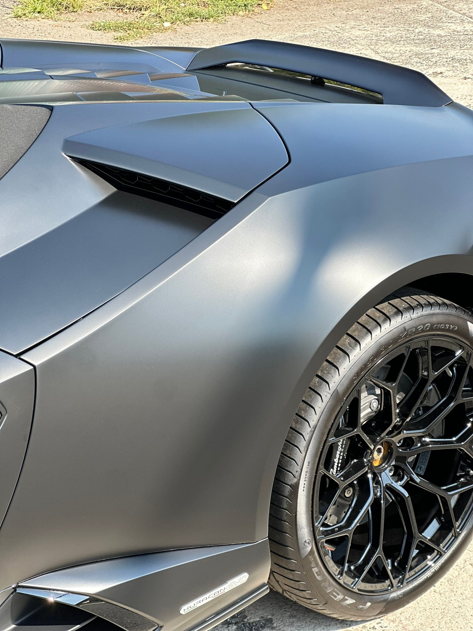 Matte black Lamborghini with black rims, parked outdoors.