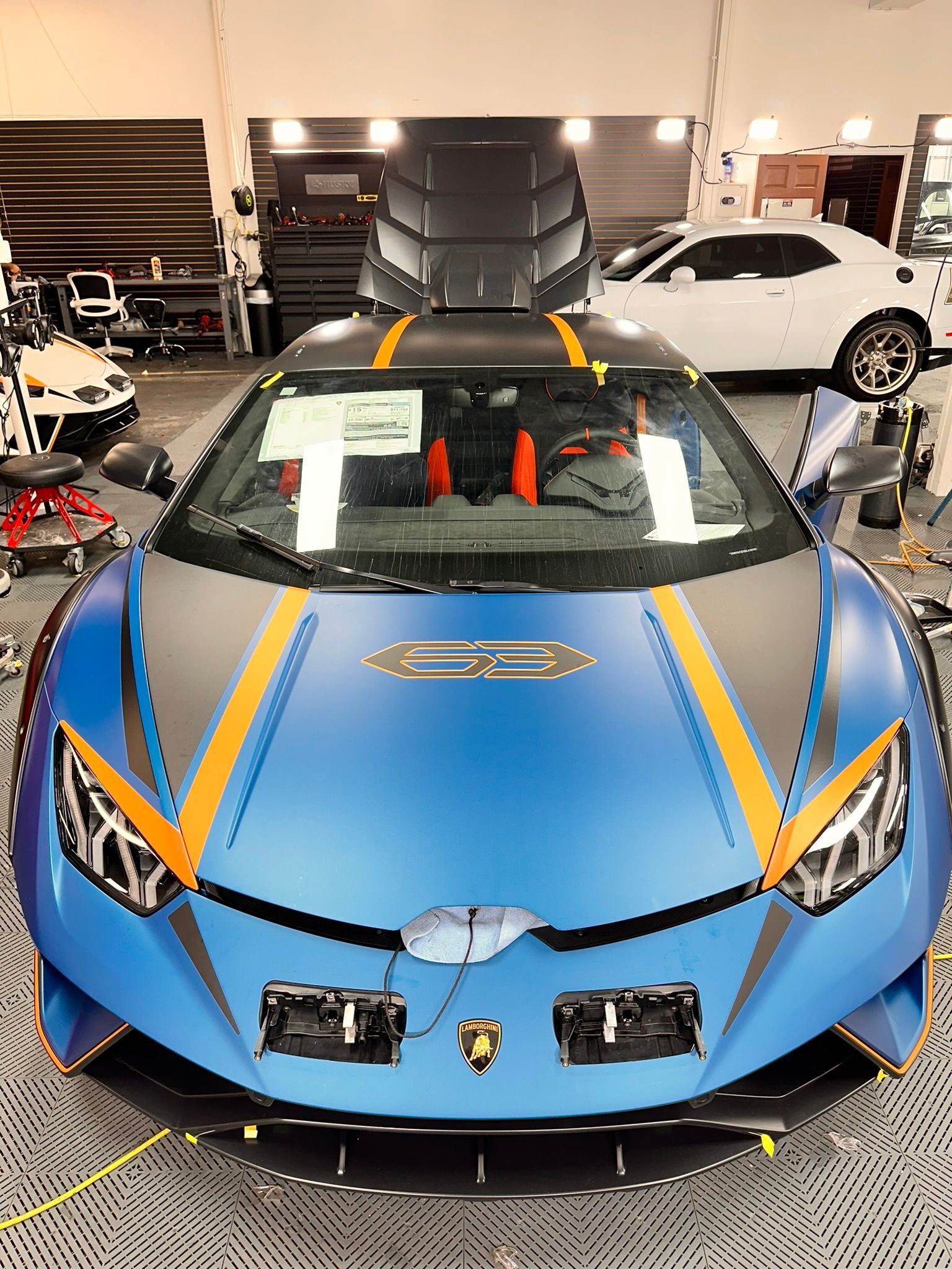 Blue Lamborghini sports car with orange stripes, inside a car shop.