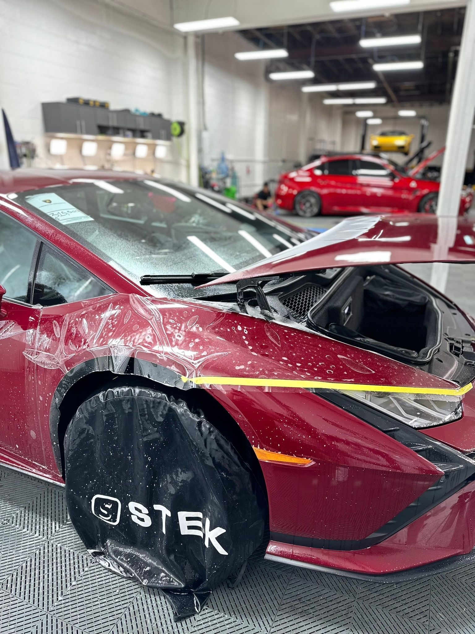 A red sports car is sitting in a garage with its hood open.