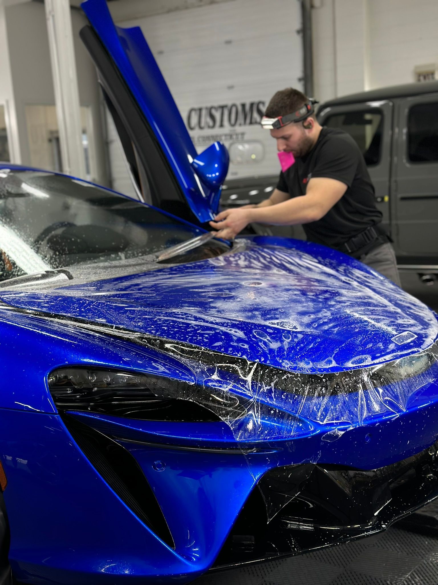 A man is wrapping a blue sports car with plastic wrap.