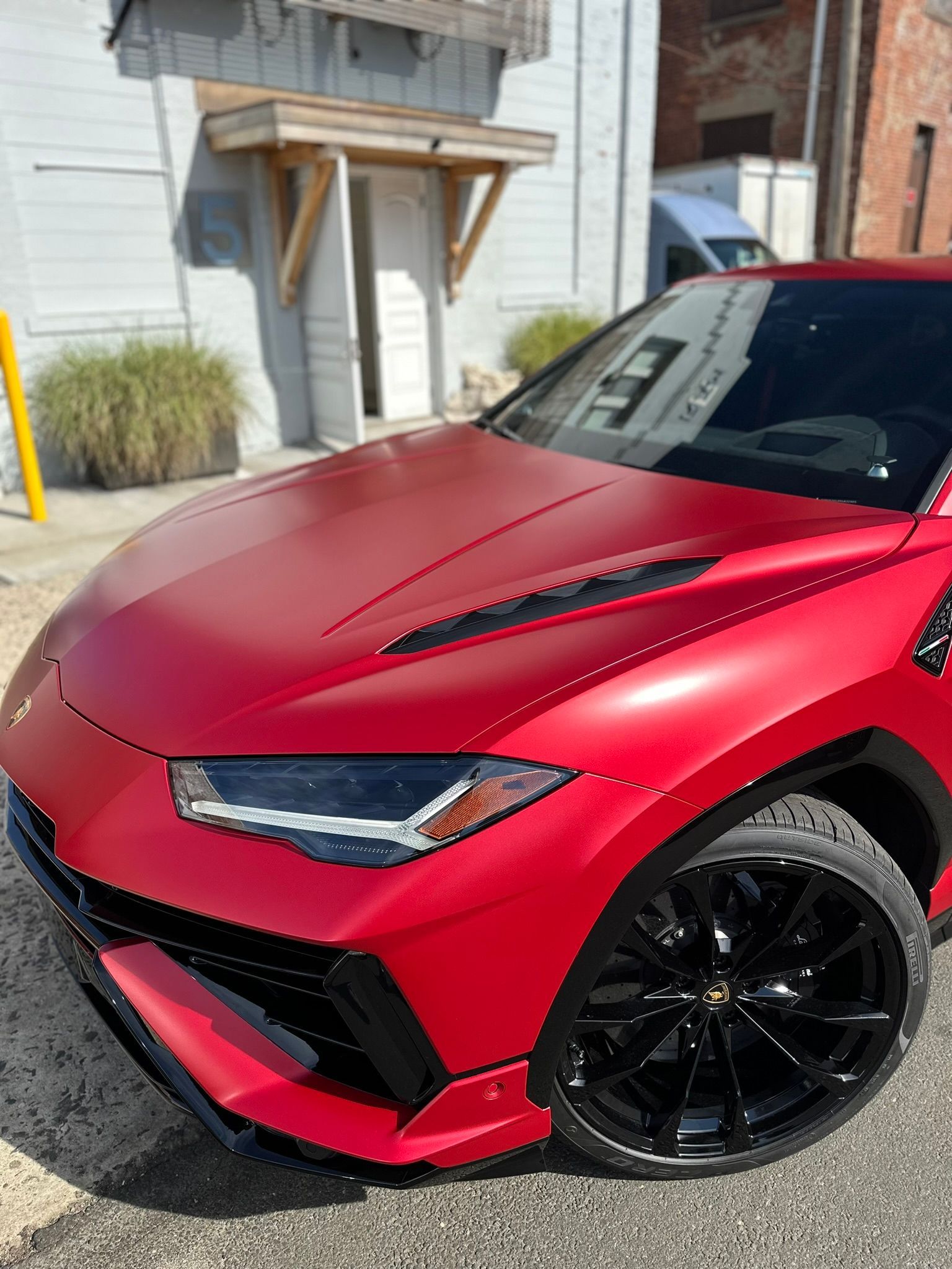 Red Lamborghini Urus parked near a building with black rims and a matte finish.