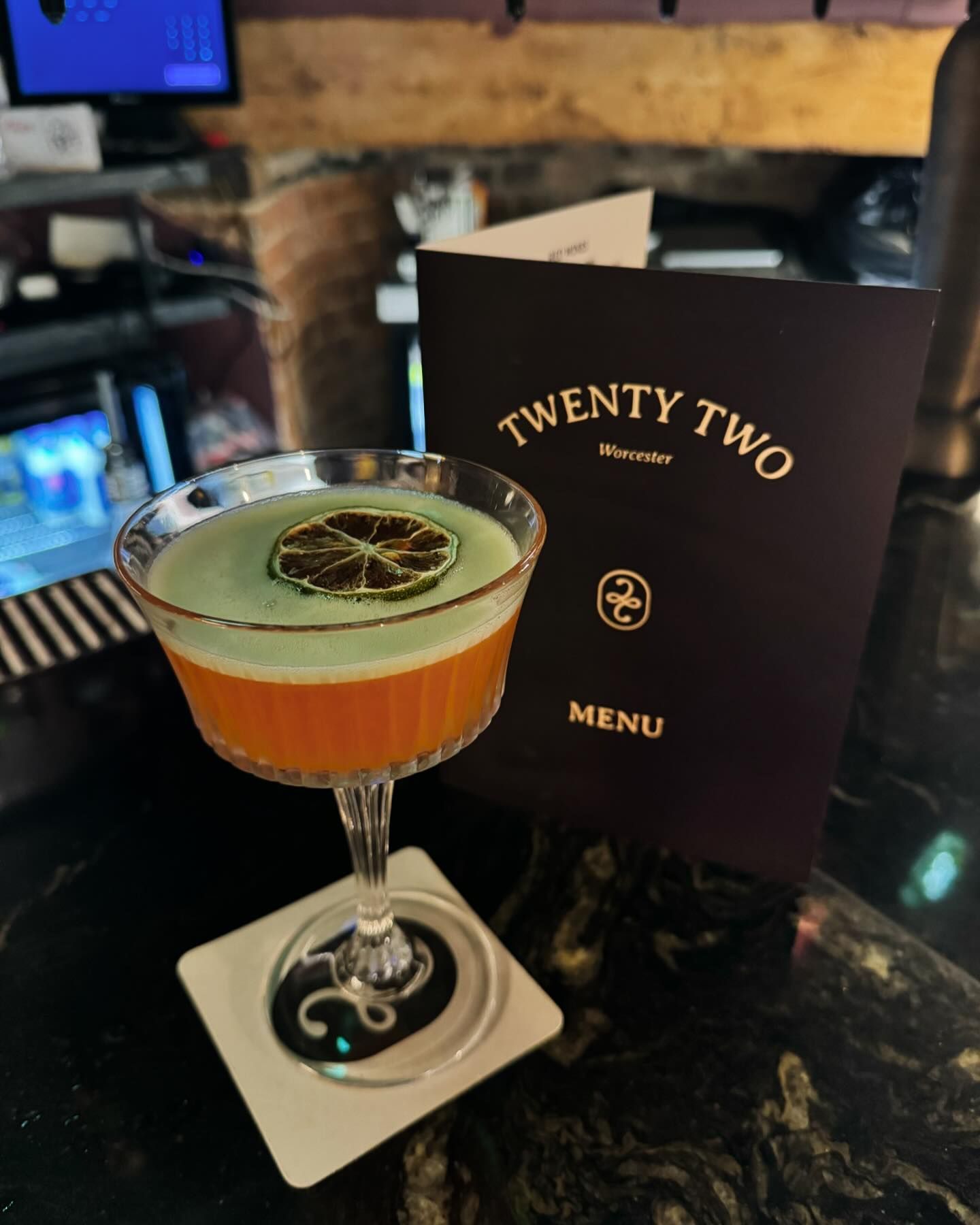 A cocktail in a martini glass next to a menu for twenty two