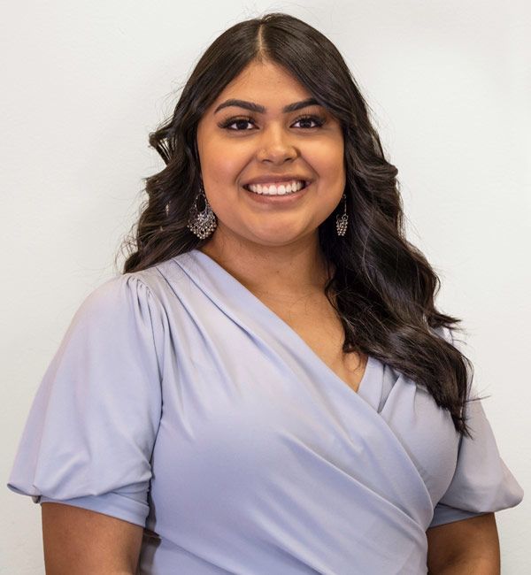 A woman wearing a purple wrap top and earrings is smiling for the camera.