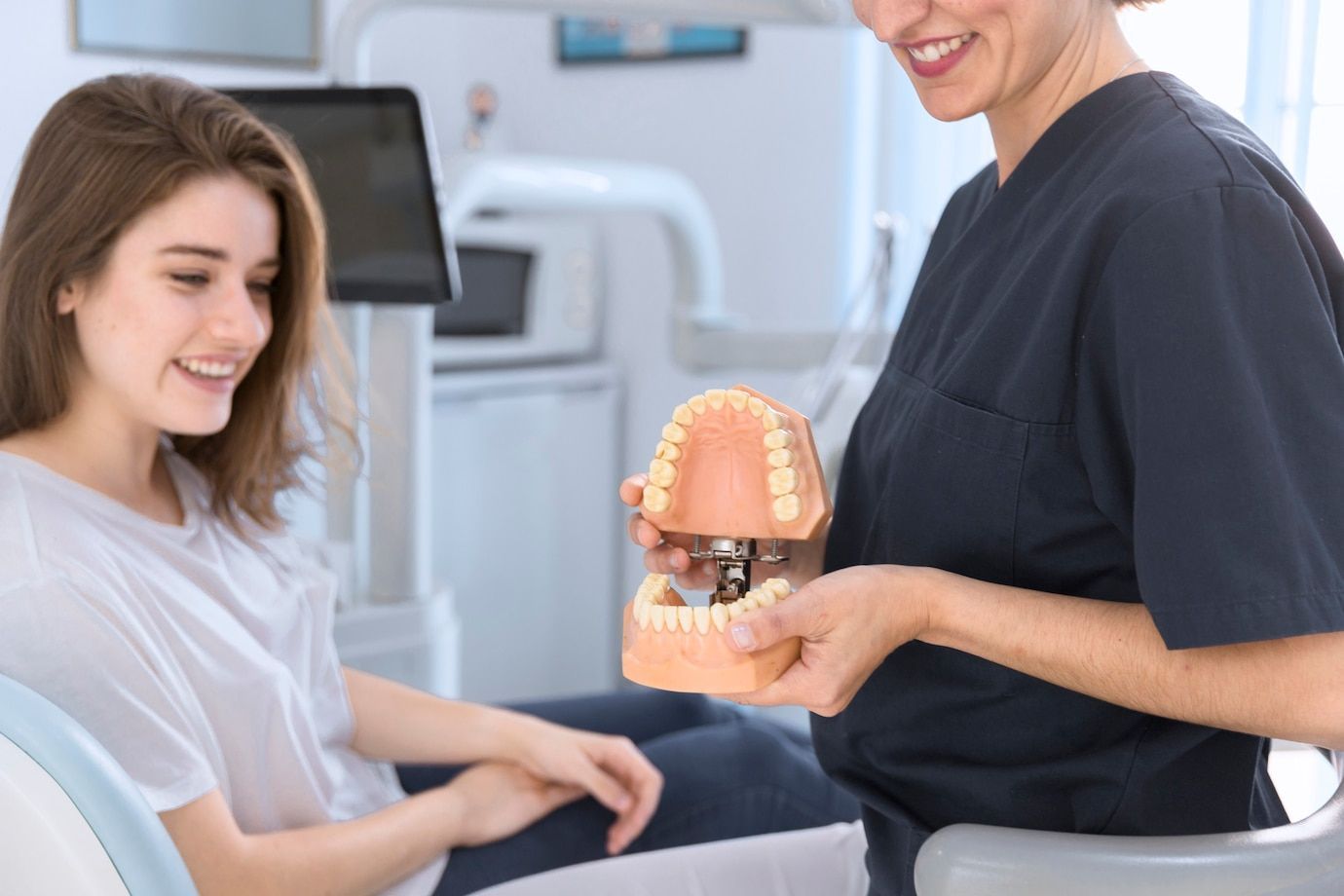 A woman is sitting in a dental chair while a dentist holds a model of her teeth.