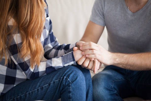 Two people on couch holding hands in close up supportive interaction setting indoors today