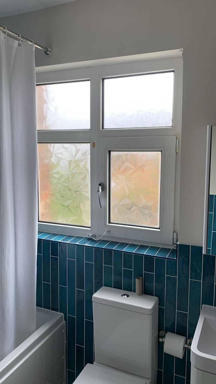 A bathroom with a toilet , sink , shower curtain and window.