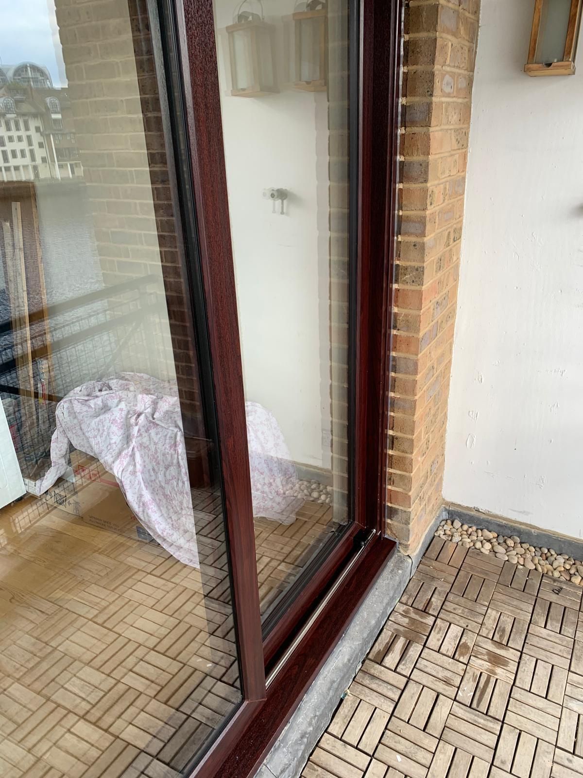 A sliding glass door is sitting on a balcony next to a brick wall.