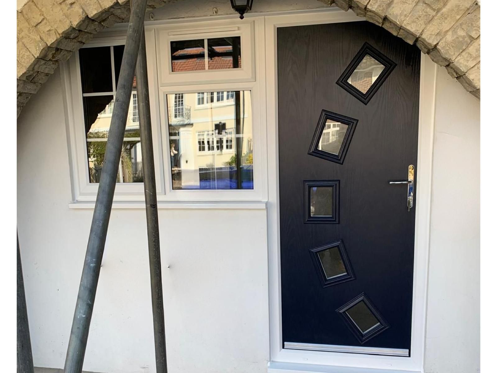 A black door with squares on it is on a white wall next to a window.