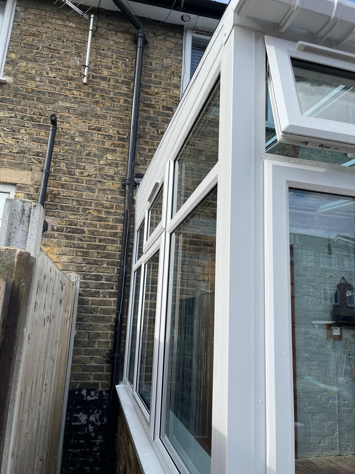 A white conservatory is sitting next to a brick building.