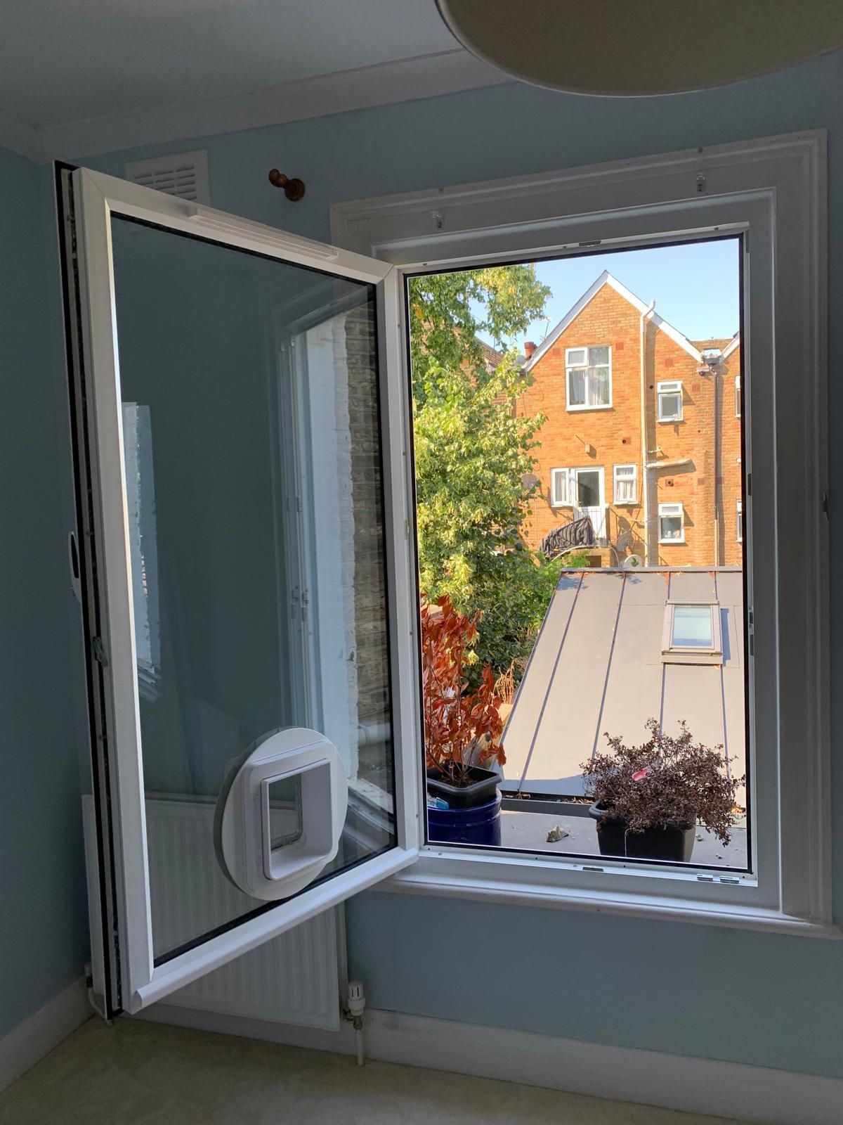 There is a cat door in the window of a room.