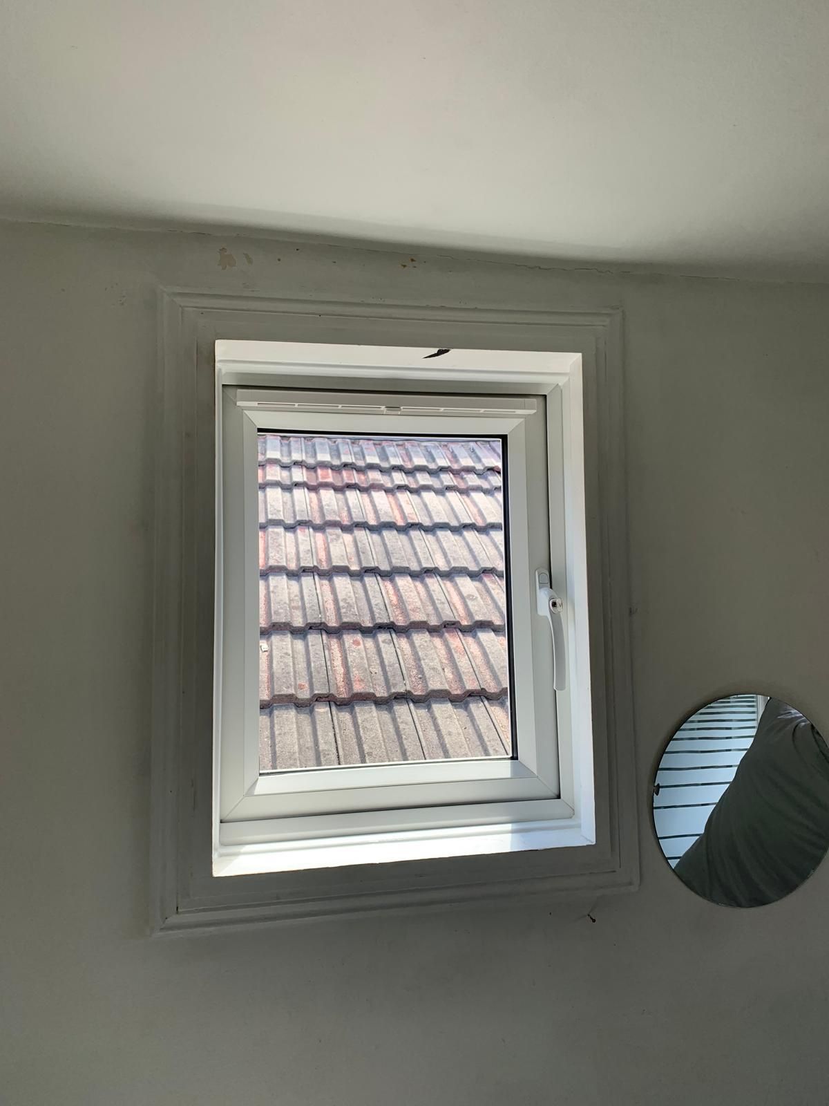 A window with a roof in the background and a mirror next to it.