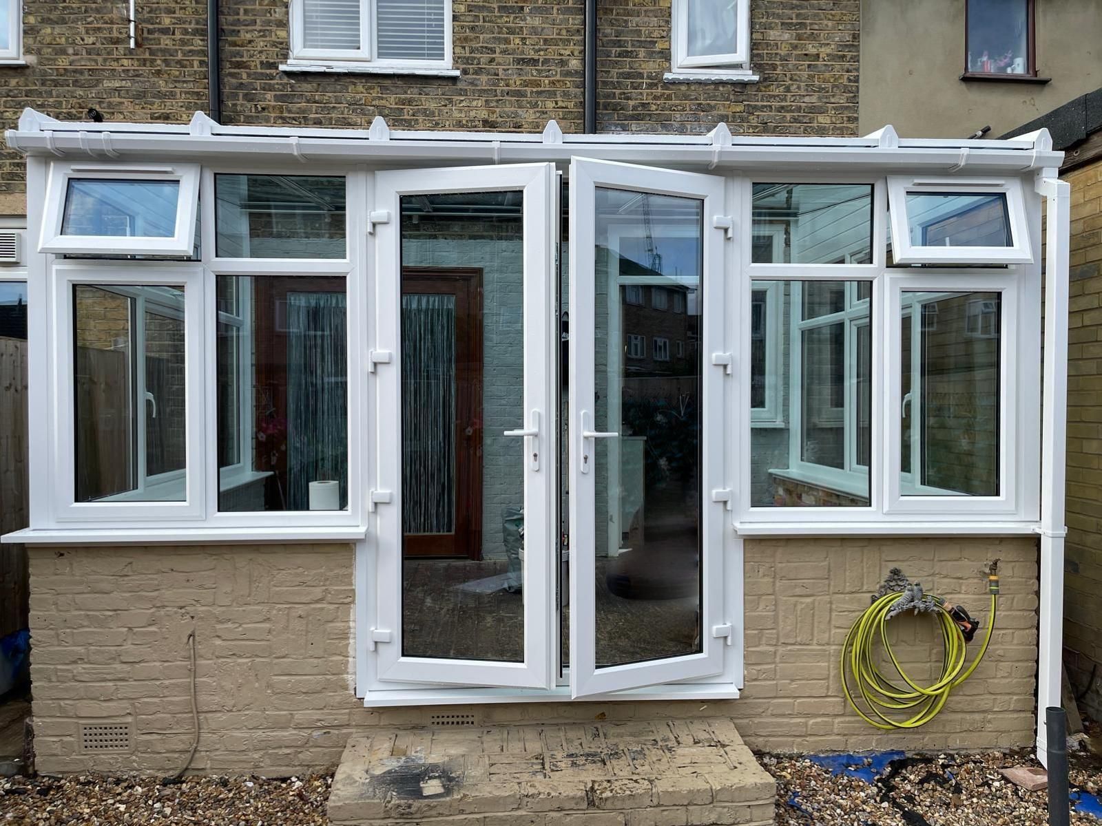 A conservatory with white doors and windows on the side of a brick house.