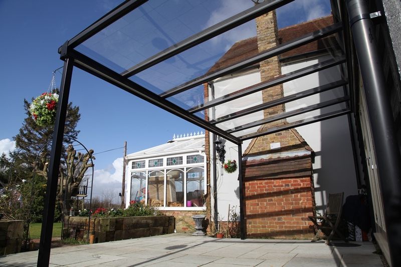 A patio with a clear roof and a brick house in the background.