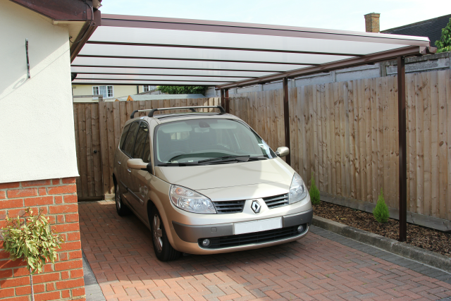 A car is parked under a canopy in a driveway