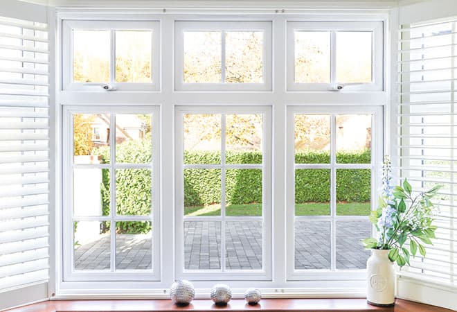 A white window with blinds and a vase of flowers on a window sill.