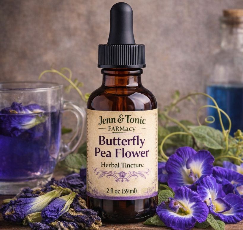 A bottle of Jenn & Tonic Butterfly Pea Flower herbal tincture surrounded by purple butterfly pea flowers and a teacup.