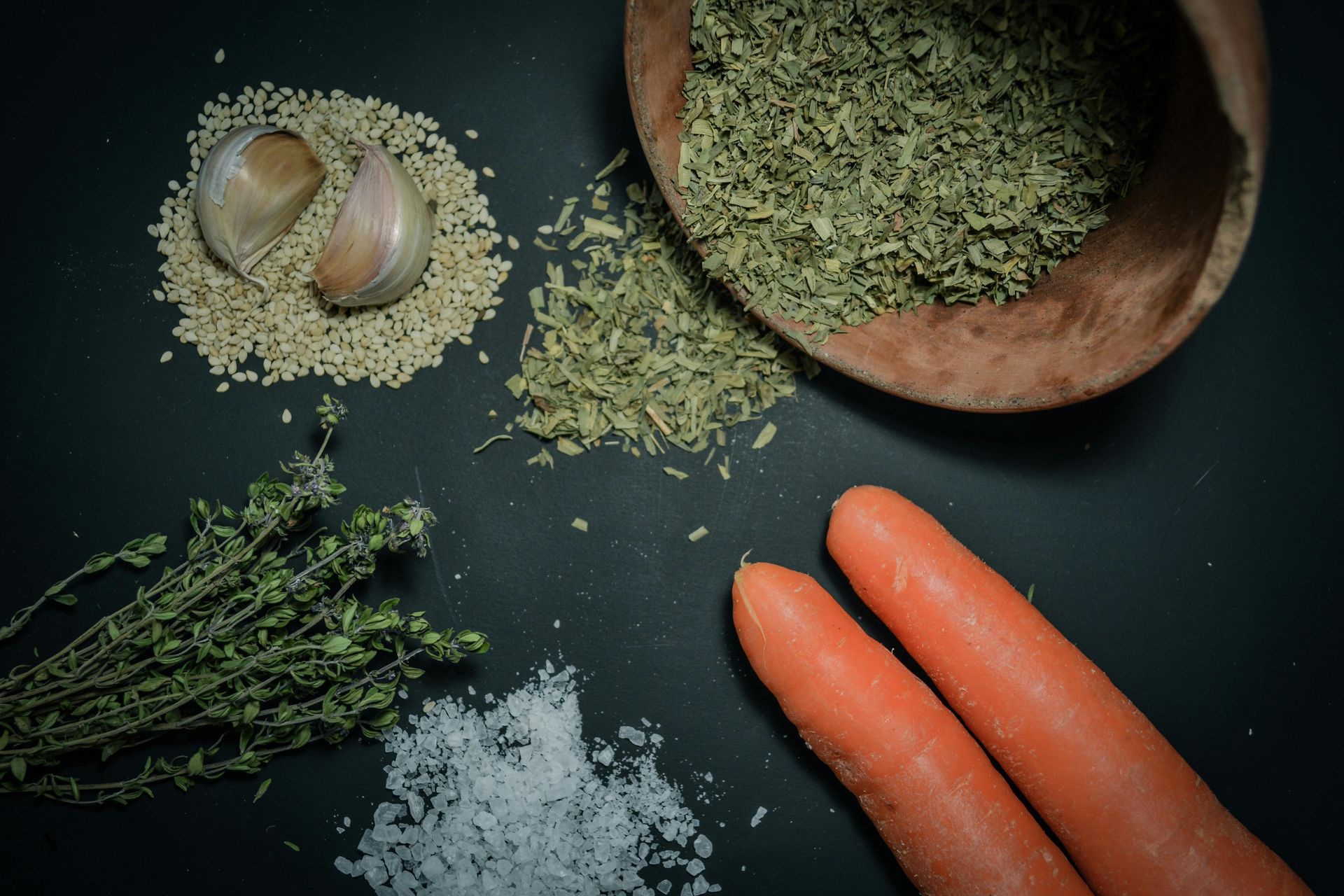 Carrots , garlic , thyme , salt and other spices are on a table.