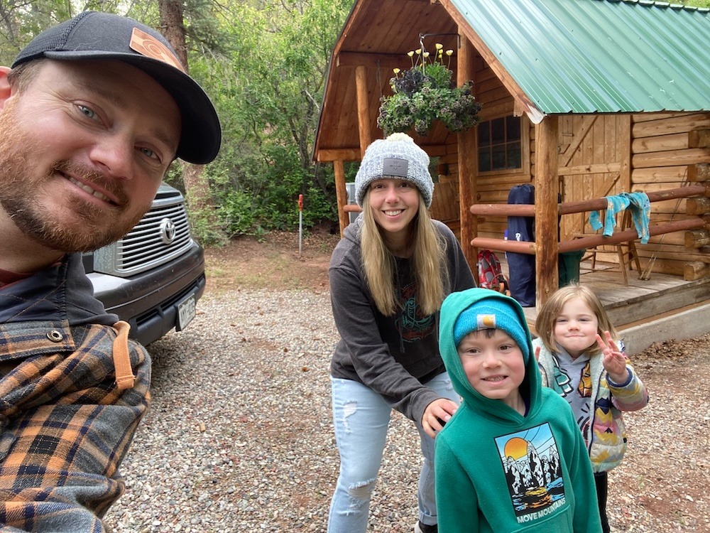 A family of four in front of a cabin in Colorado surrounded by trees