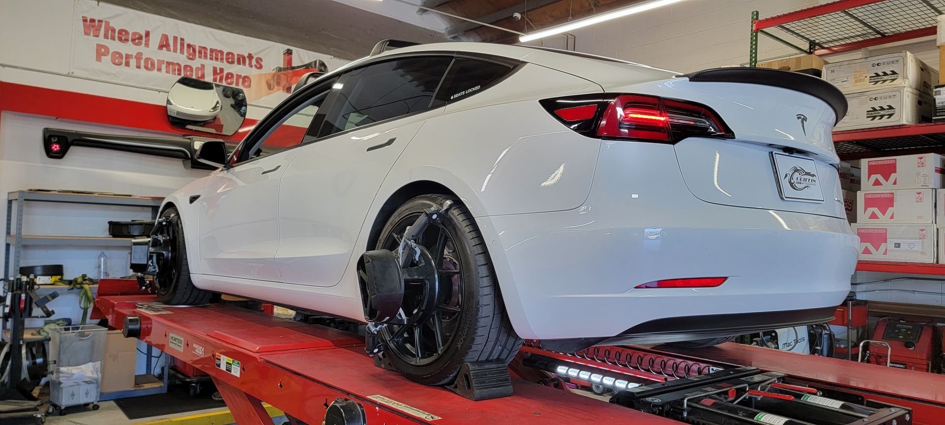 A white tesla model 3 is sitting on a lift in a garage.