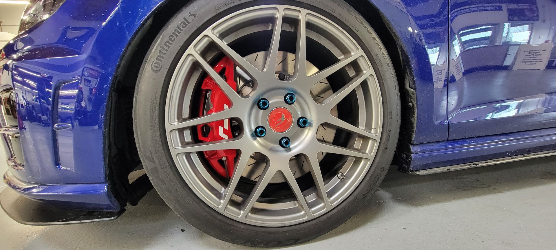 The front wheel of a blue car with red brake calipers | Griffin Motorwerke