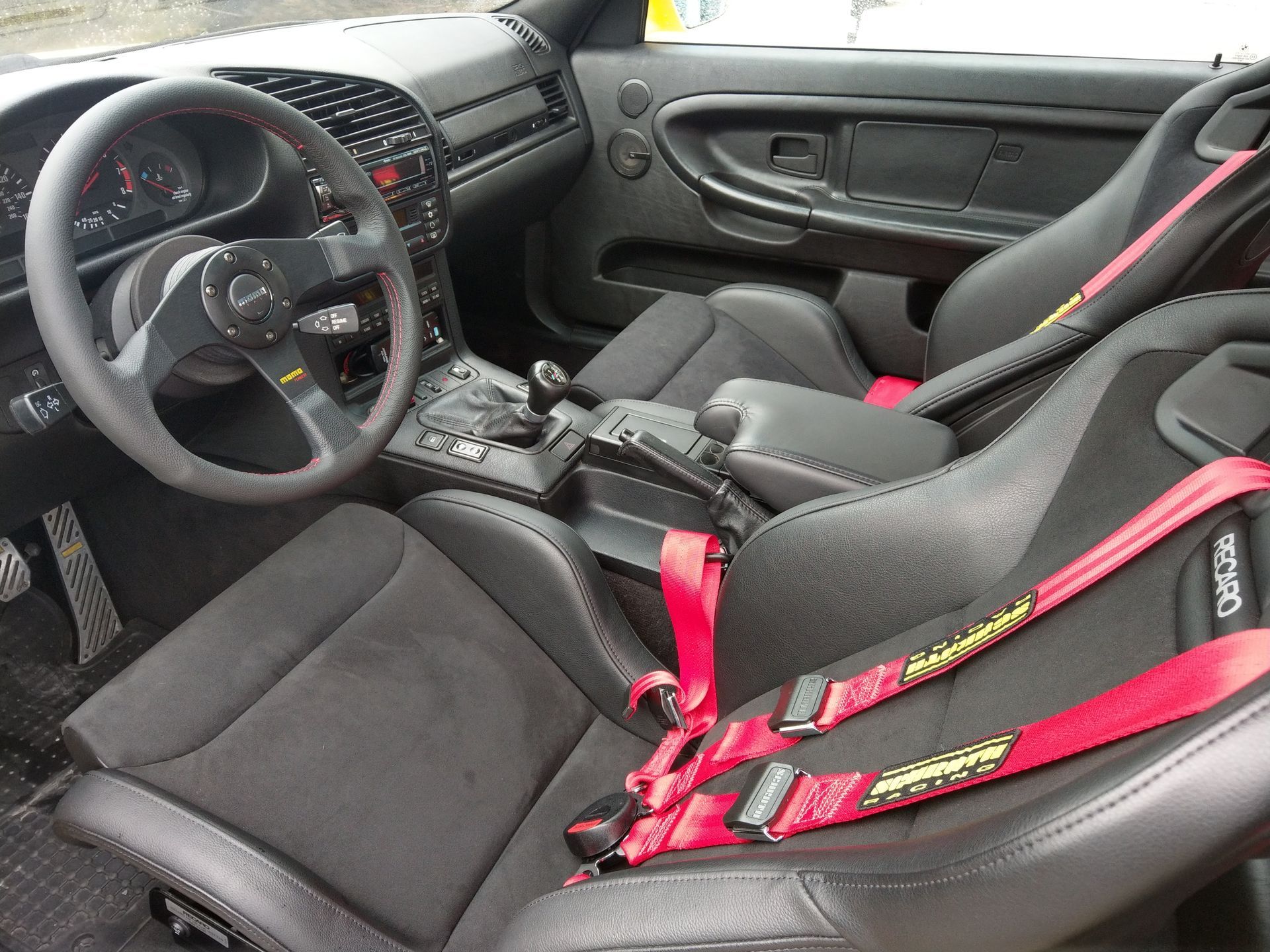 The inside of a car with black seats and red seat belts | Griffin Motorwerke