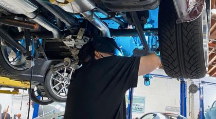 A man is working on the underside of a car in a garage | Griffin Motorwerke