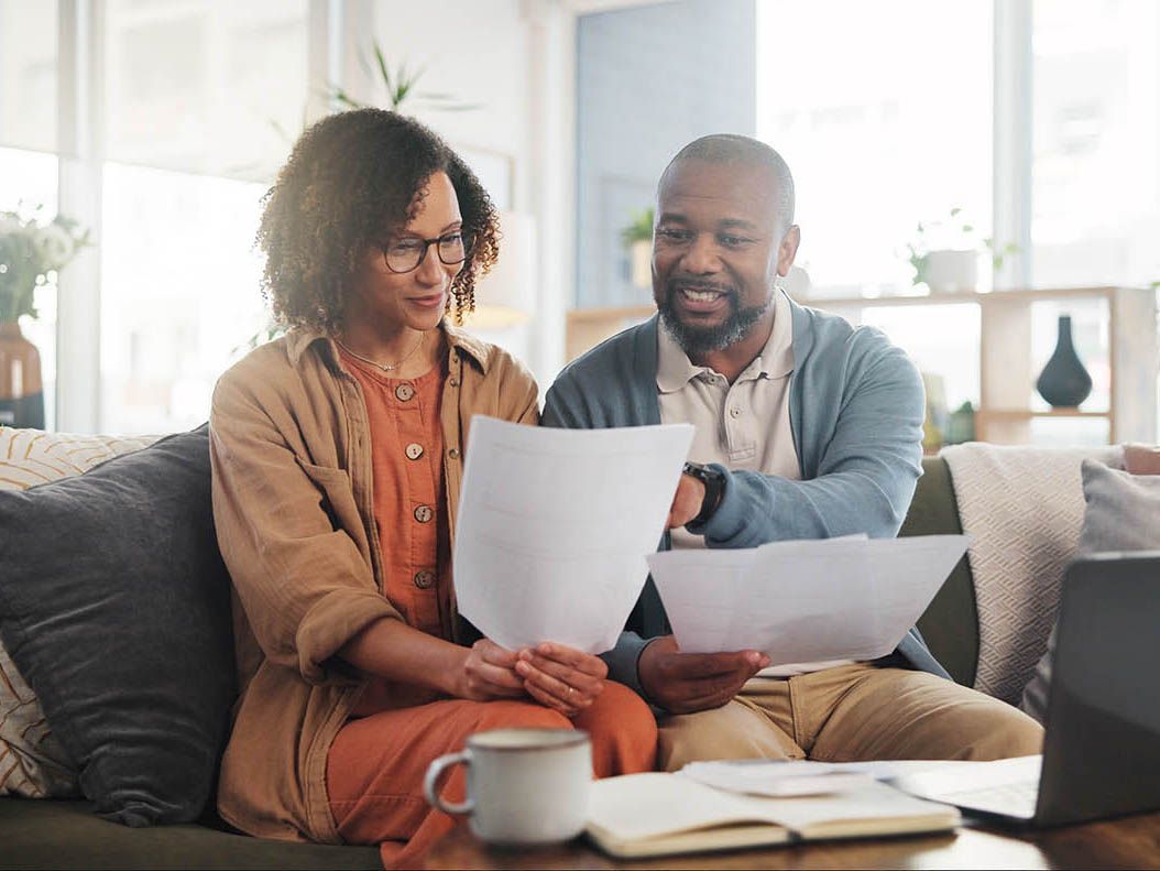 A man and a woman are sitting on a couch looking at papers.