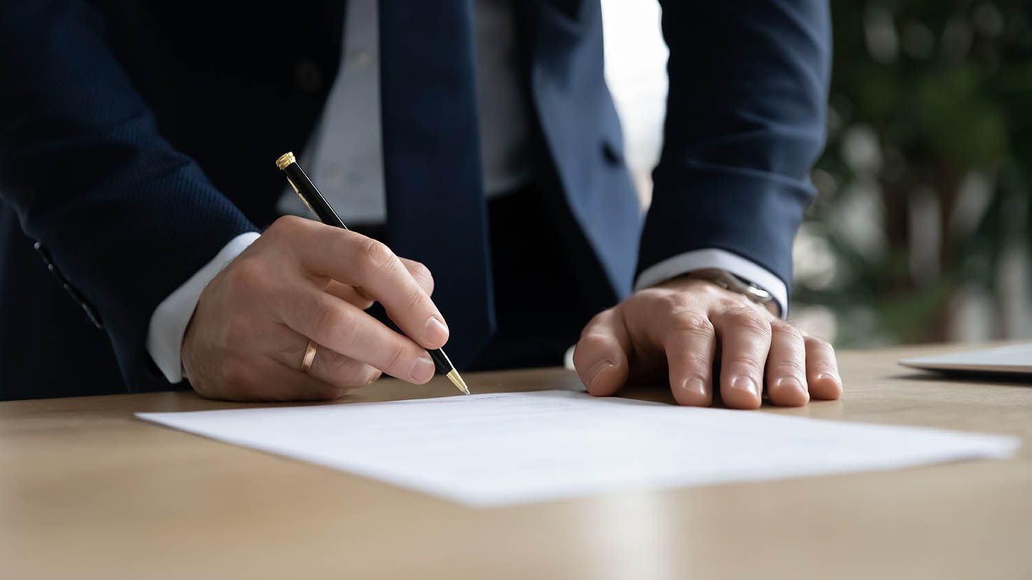 A man in a suit is writing on a piece of paper with a pen.