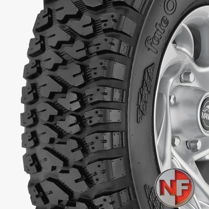 Primer plano de un neumático todoterreno negro con banda de rodadura gruesa sobre una llanta plateada.